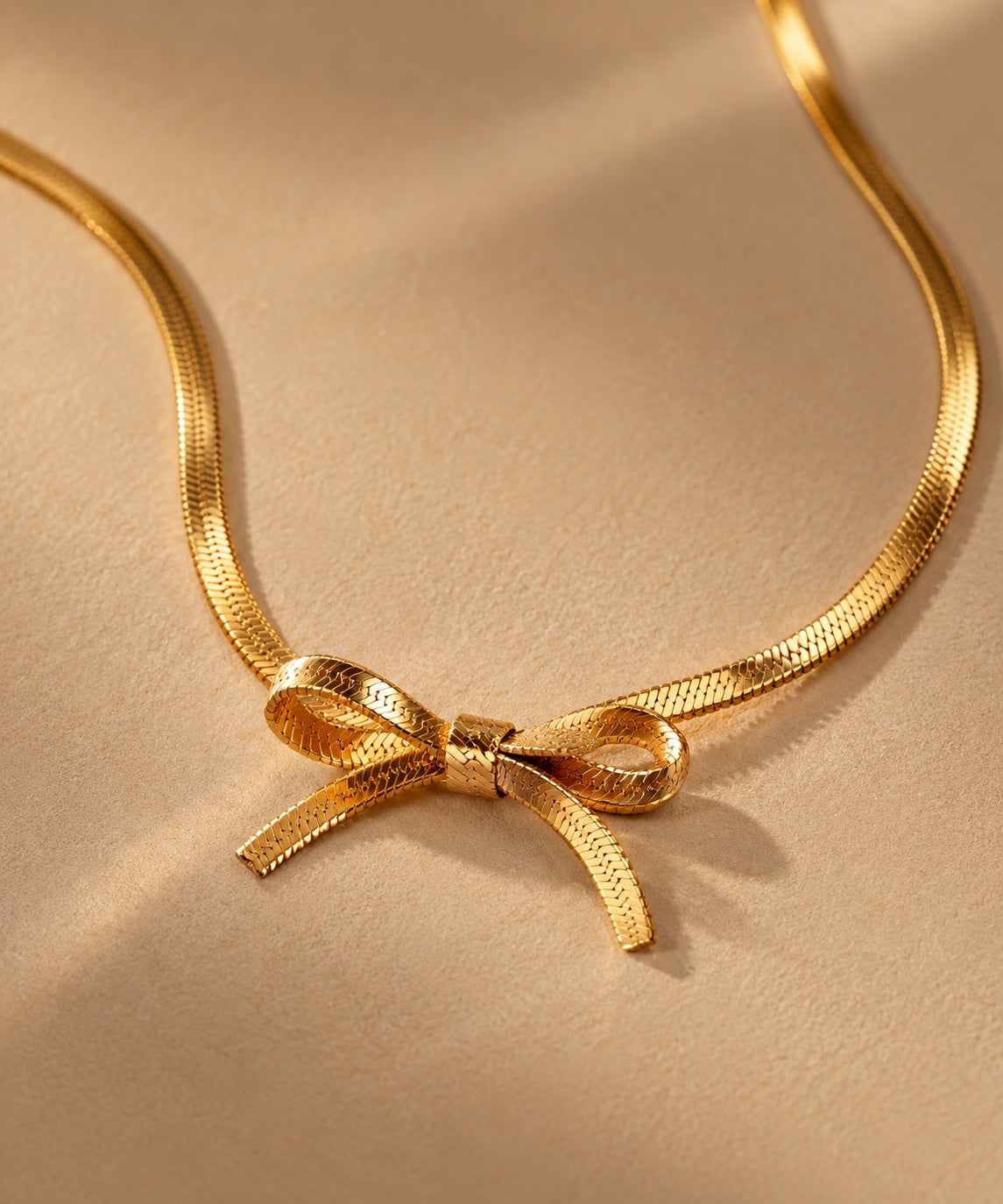 Close up detail of gold plated bow pendant necklace on warm beige background