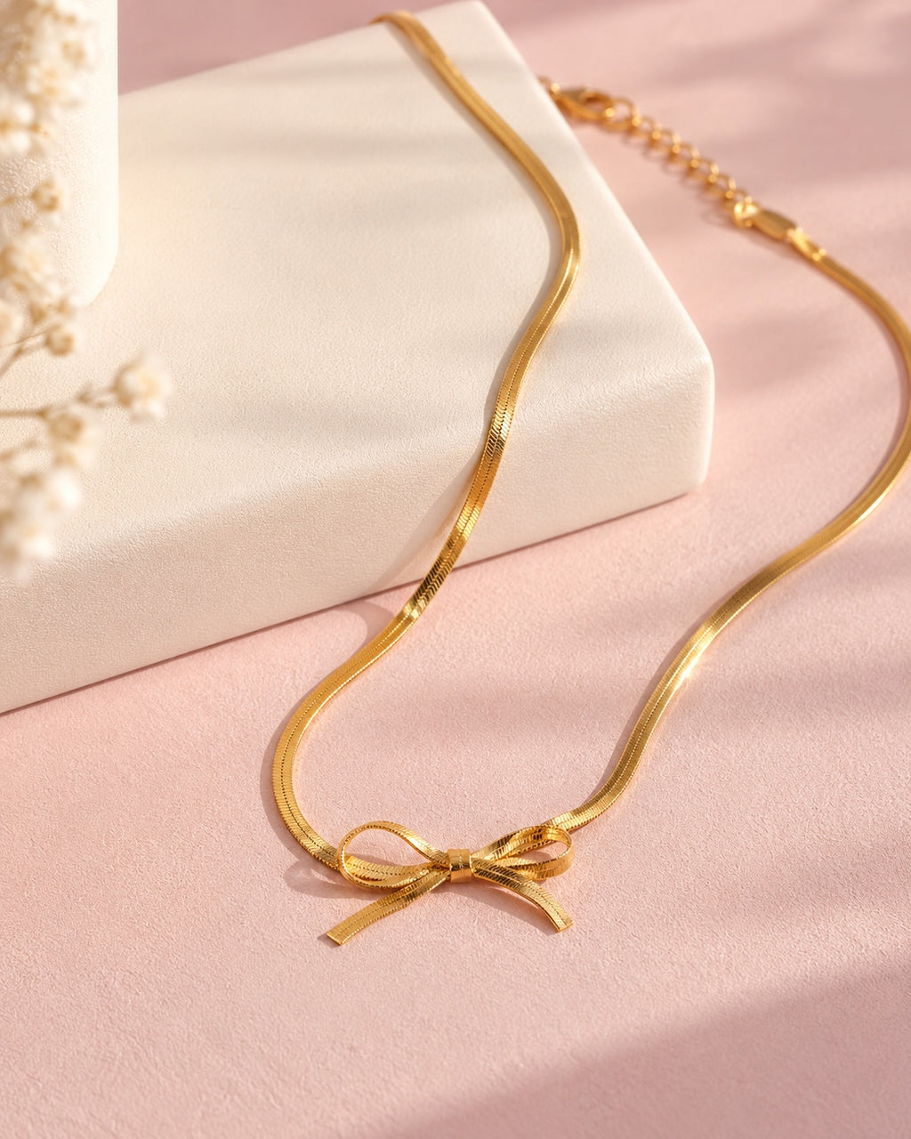 Gold bow necklace displayed on an ivory jewelry stand against blush pink background
