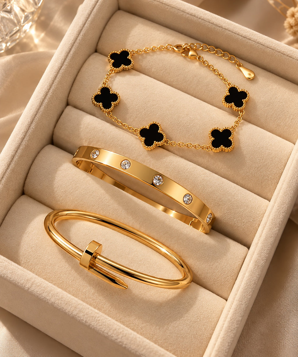Set of three gold-tone bracelets arranged in a cream jewellery tray