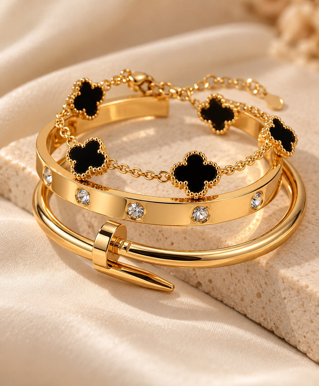 Close-up of three gold-tone bracelets with black clover and crystal details