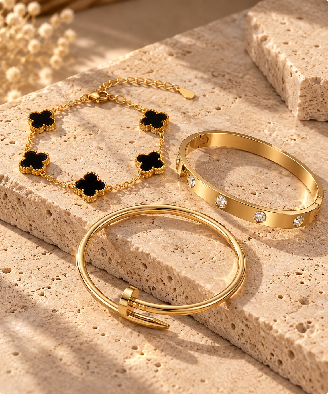 Three gold-plated bracelets displayed on a beige stone surface