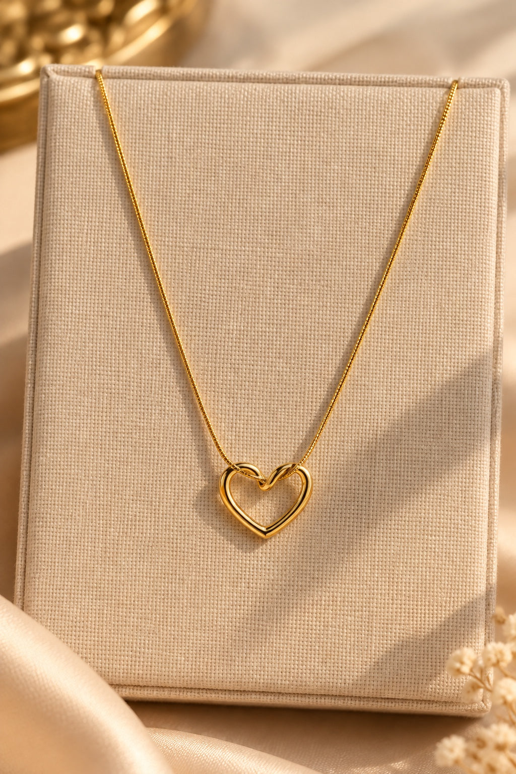 Gold-plated heart pendant necklace displayed on a beige jewellery stand