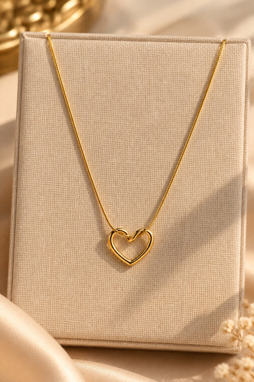 Gold-plated heart pendant necklace displayed on a beige jewellery stand