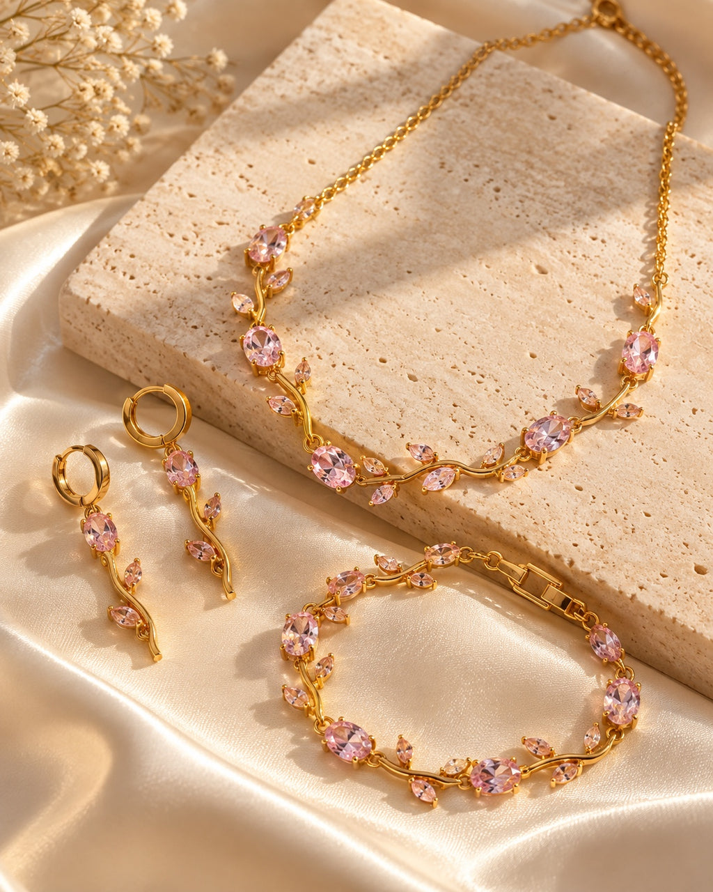 Pink floral gold-tone jewellery set styled on a warm stone surface